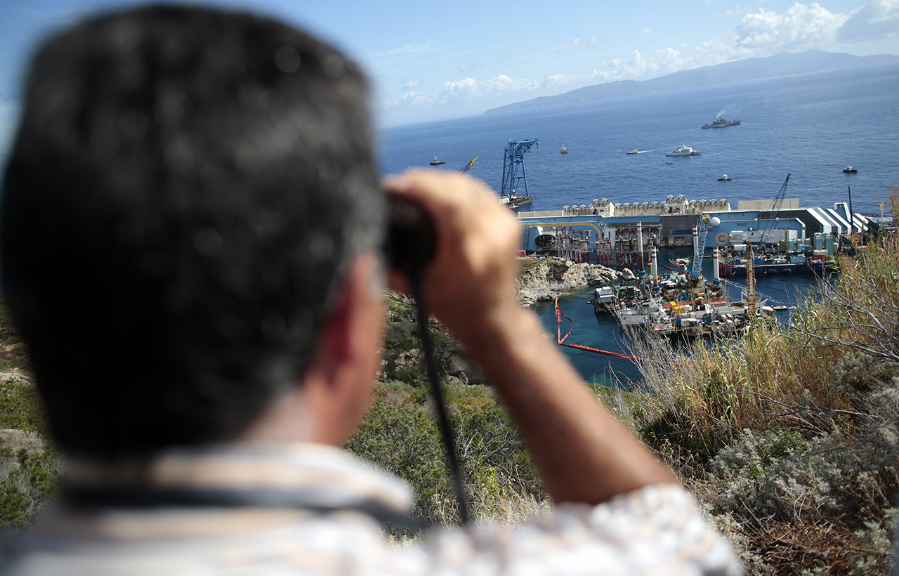 A person looks on with binoculars as the capsized cruise liner Costa Concordia lies on its side next to Giglio Island