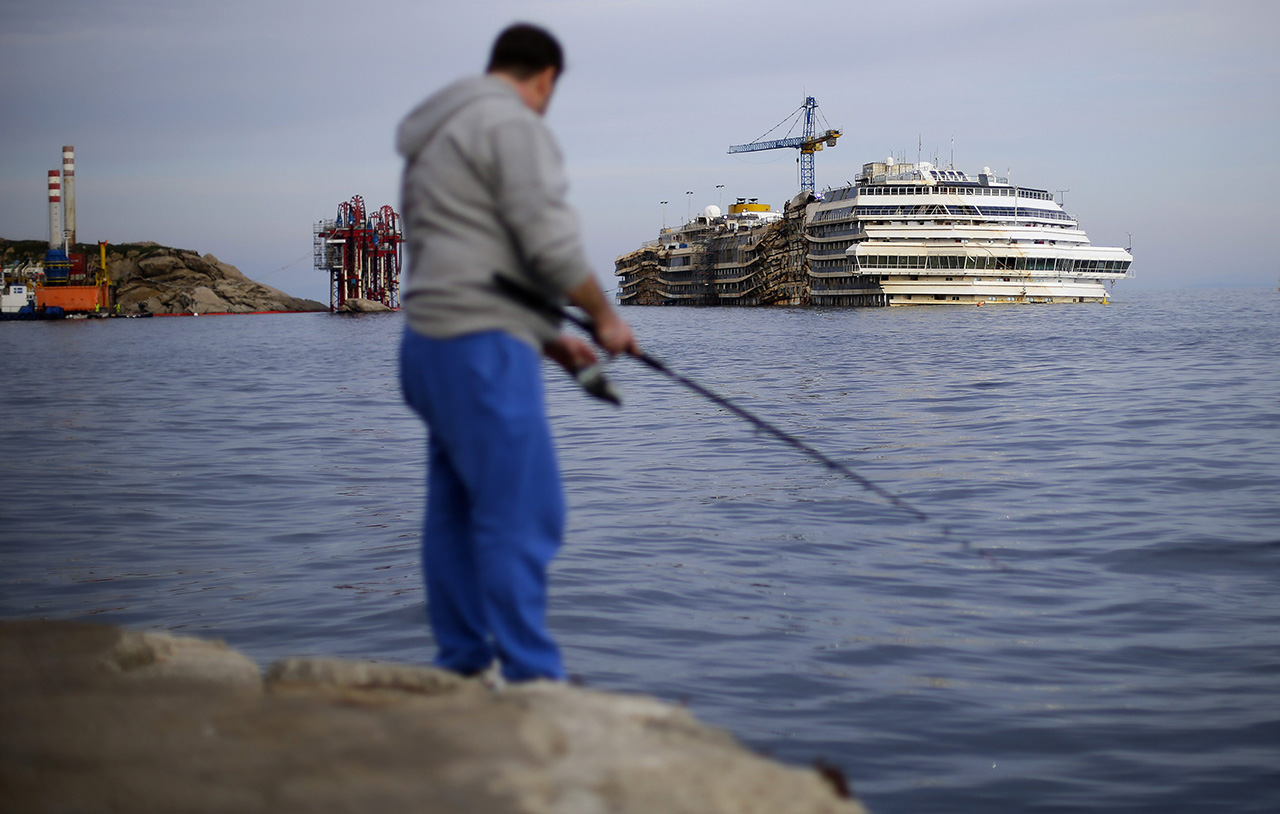 A man fishes in front of the cruise liner Costa Concordia during the "parbuckling" operation outside Giglio harbour