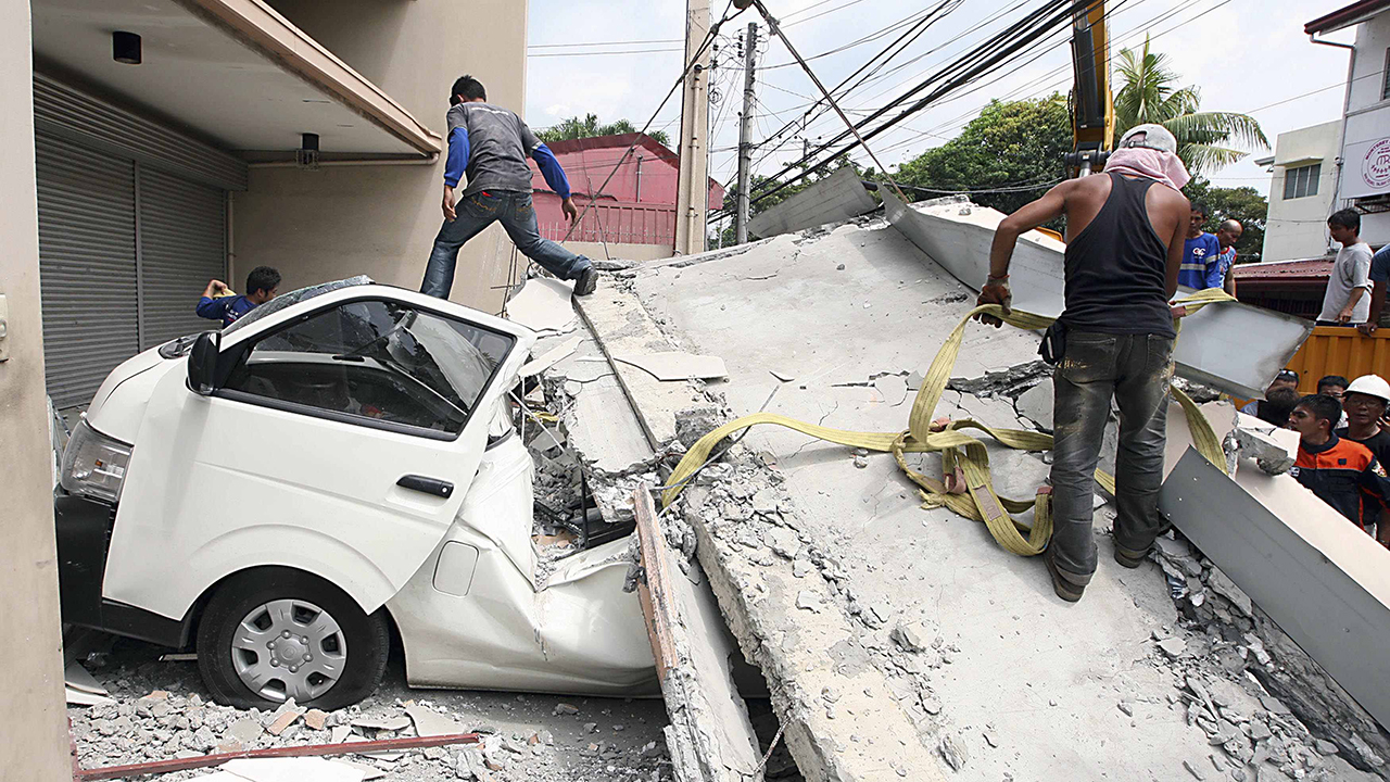 Workers use a crane to lift up concrete block that fell on a car after buildings collapsed during an earthquake in Cebu city