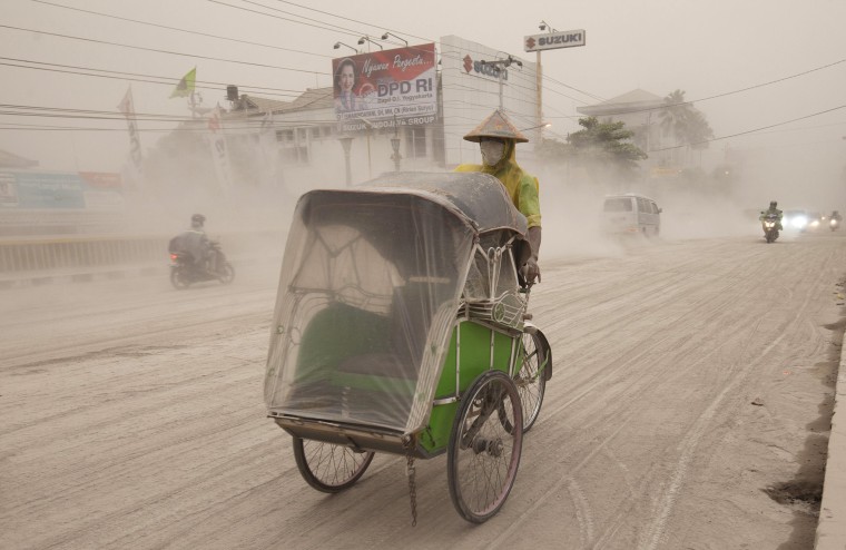 A man wears a mask as he rides a becak, a kind of rickshaw, on a road covered with from Mount Kelud, in Yogyakarta