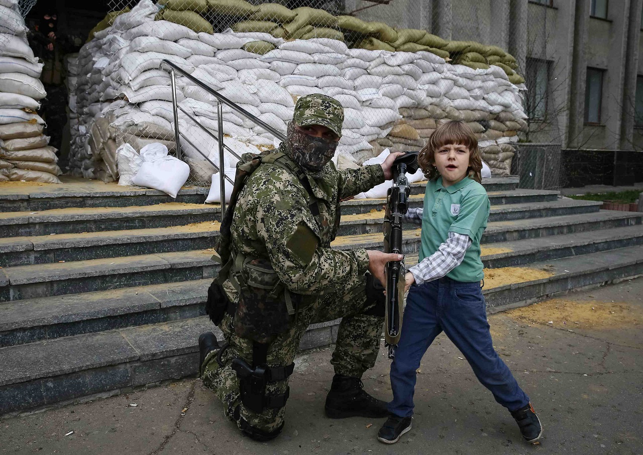 A pro-Russian armed man allows a local boy to hold a machine gun, while standing guard outside the mayor's office in Slaviansk